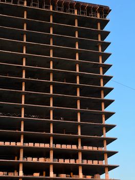 Modern high-rise building under construction, showcasing concrete layers and blue sky backdrop.