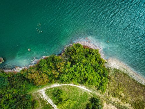 Free Aerial shot of lush green coastal vegetation meeting a serene, crystal-clear body of water. Stock Photo