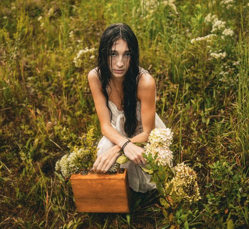Free Young woman squatting in a wild meadow holding a suitcase and flowers, captured in Atlanta, GA. Stock Photo