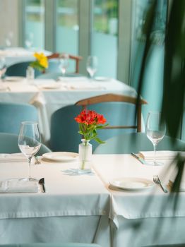 A beautifully set restaurant table with wine glasses and flowers in a light-filled interior.