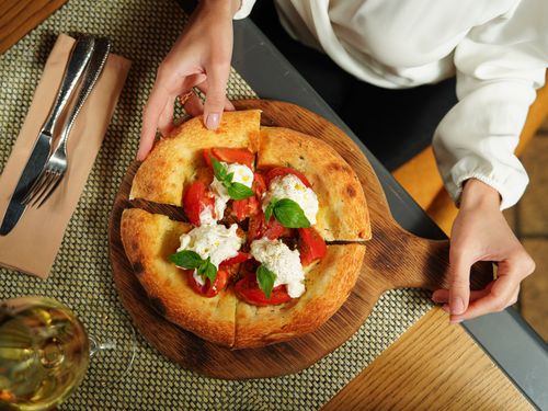 Free Delicious Italian pizza with tomatoes and basil, held by hands in a cozy restaurant setting. Stock Photo