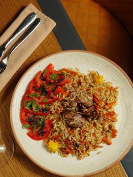 Top view of a savory grilled meat and seasoned rice dish garnished with fresh tomatoes.