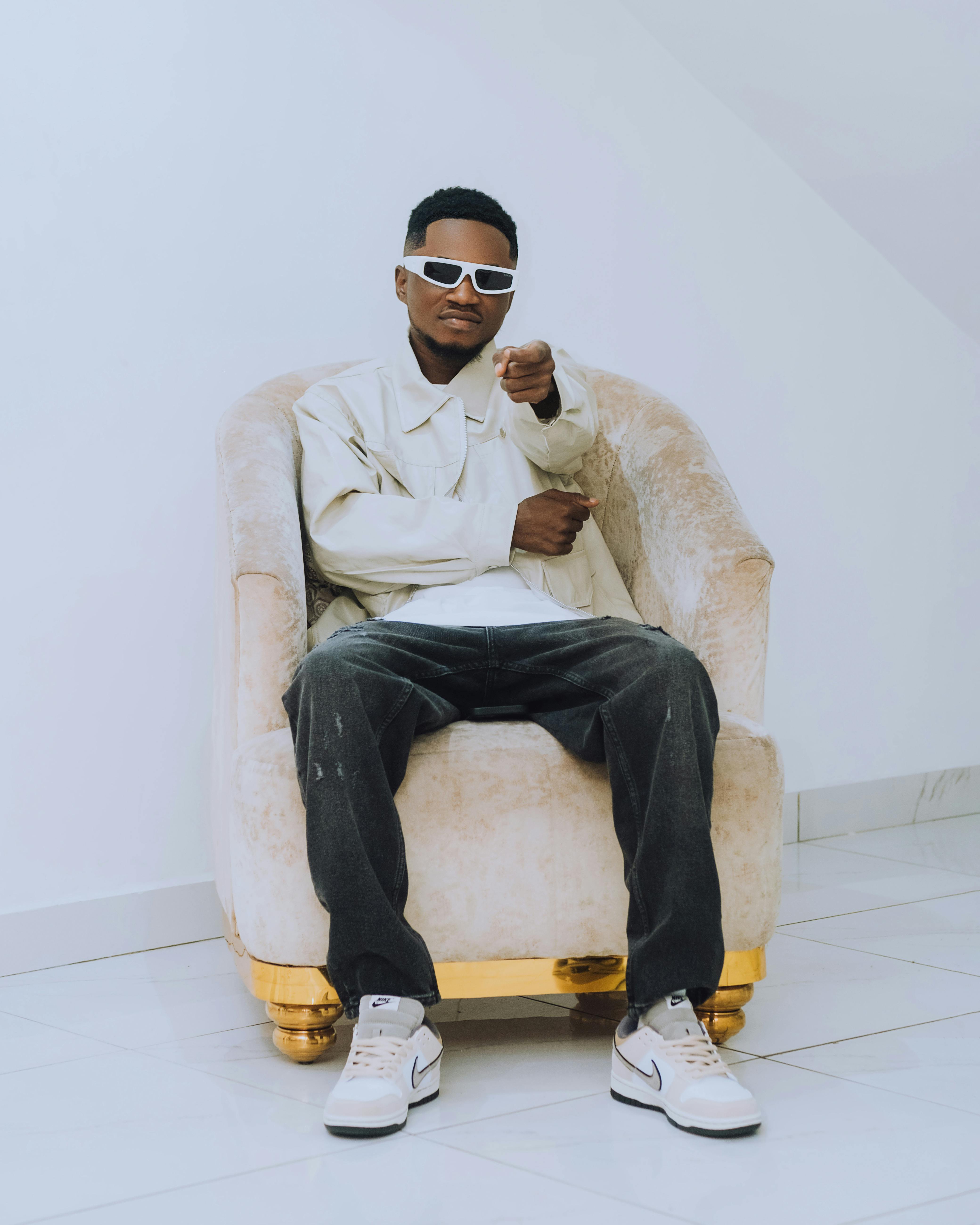 Fashionable man with sunglasses posing in plush armchair on a white background.