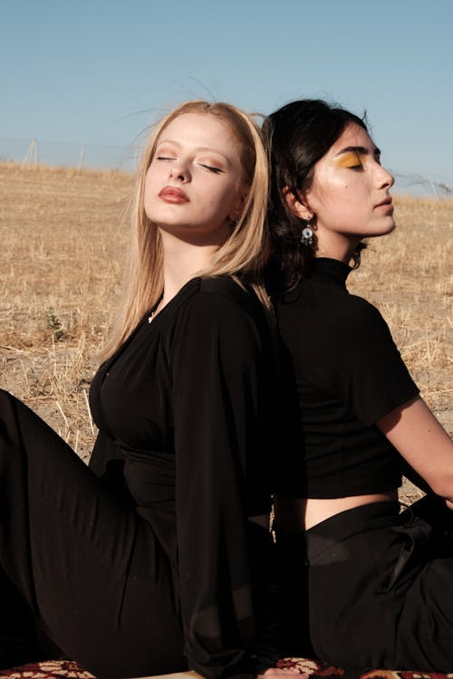 Blonde and Brunette Woman Sitting on Rural Field