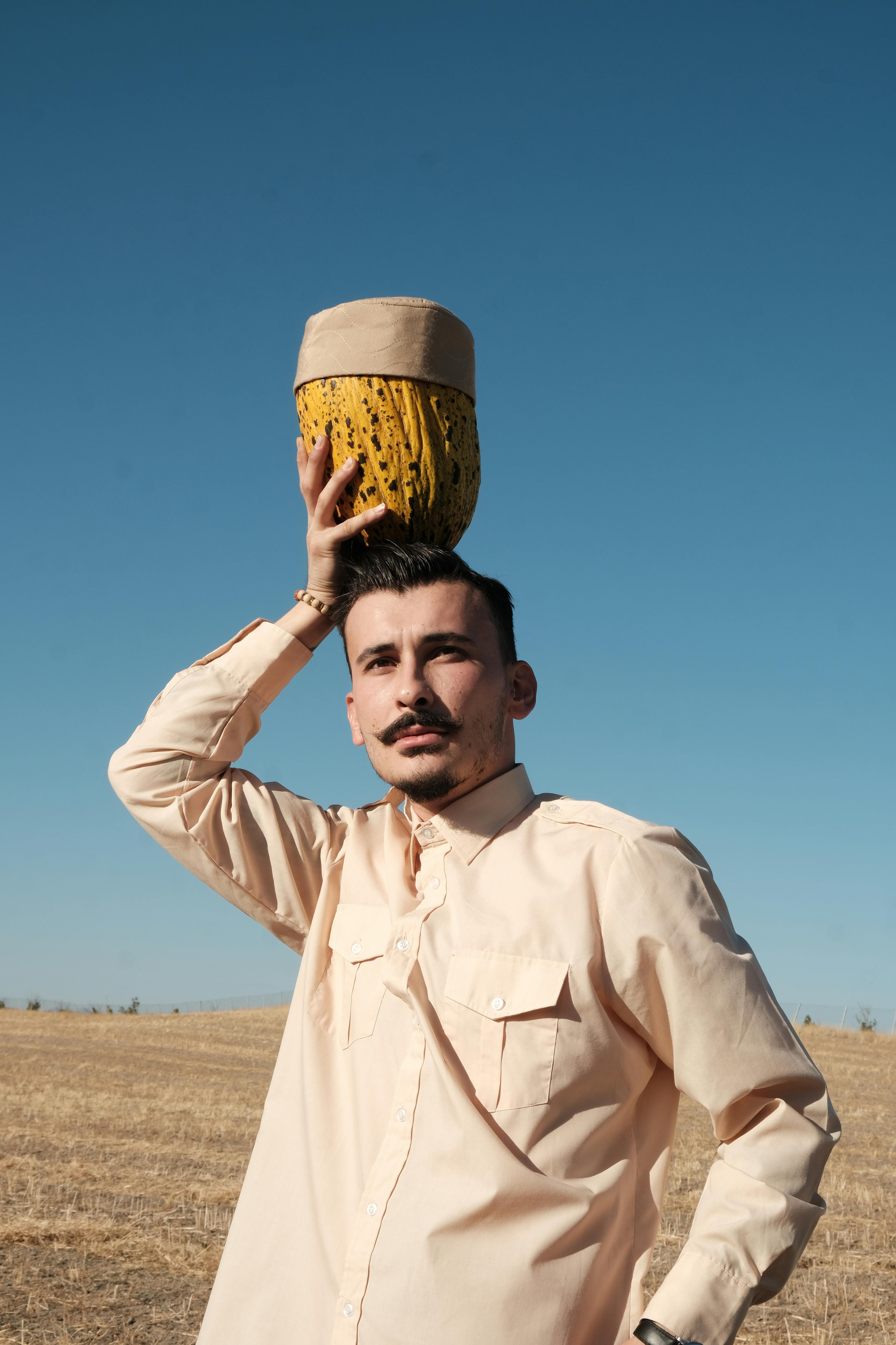 A Man Standing on a Field and Holding a Melon on His Head · Free Stock