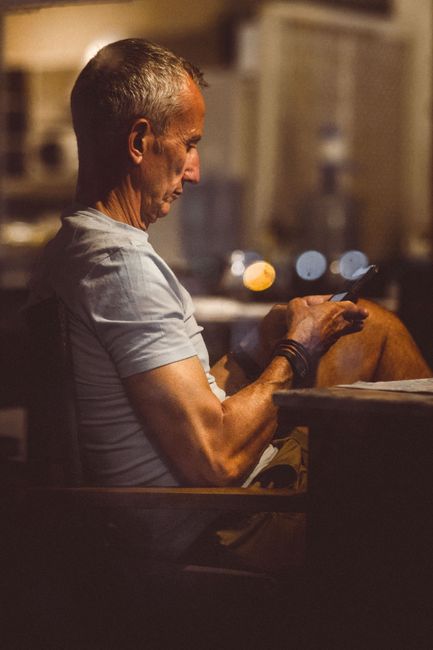 An older man sits comfortably, focused on his smartphone in a softly lit room.