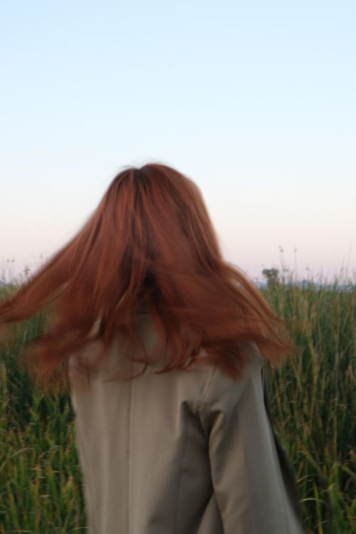 Free A red-haired person standing in a grass field, turning away during summer. Stock Photo