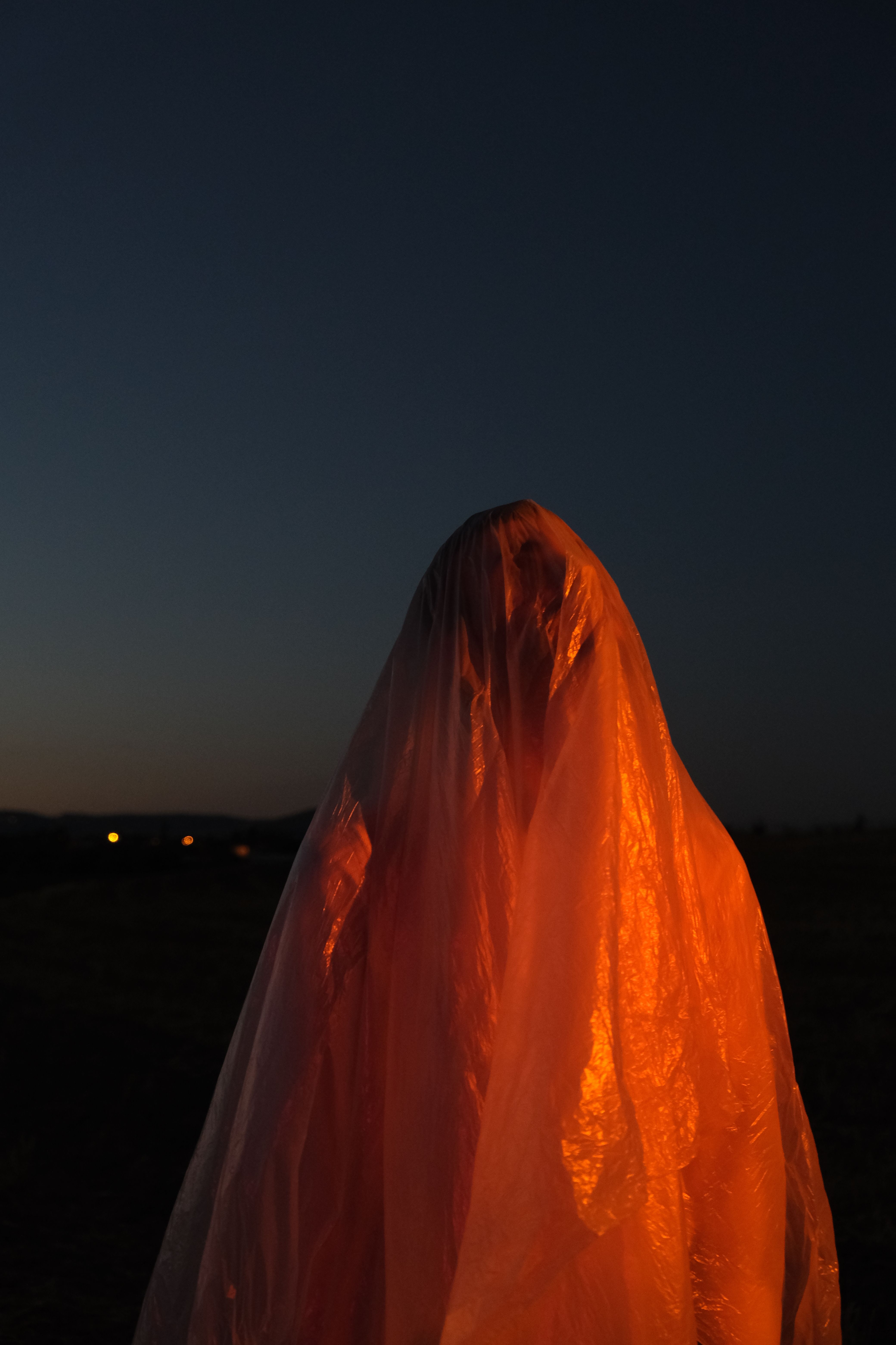 A mysterious figure shrouded in a translucent cloak, illuminated against a twilight sky.