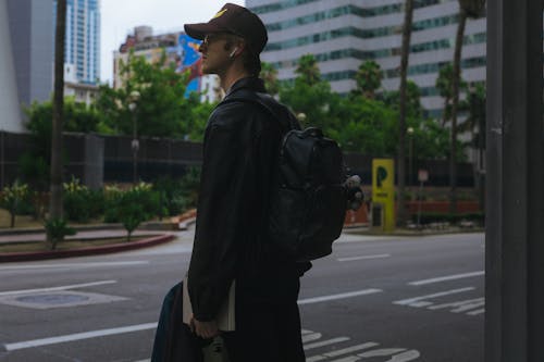 Young Man in a Leather Jacket with a Backpack Standing on the Street