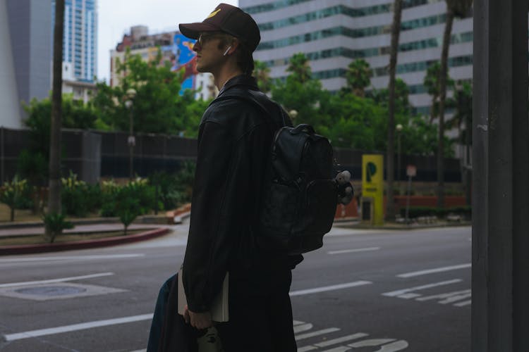 Young Man In A Leather Jacket With A Backpack Standing On The Street