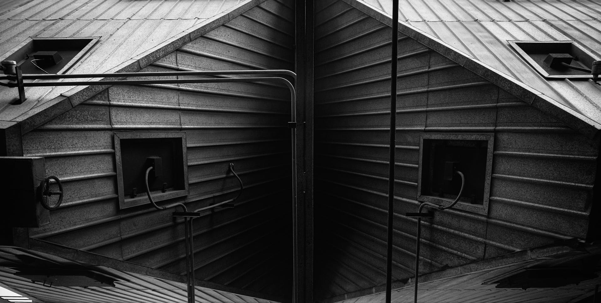 A symmetrical industrial roof structure with pipes and metal sheets in black and white.