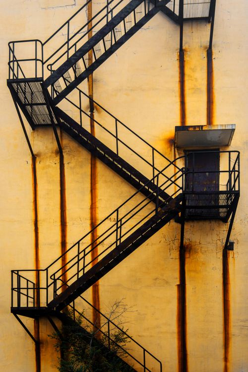 Free Vertical shot of a rusty metal fire escape against a yellow wall. Stock Photo