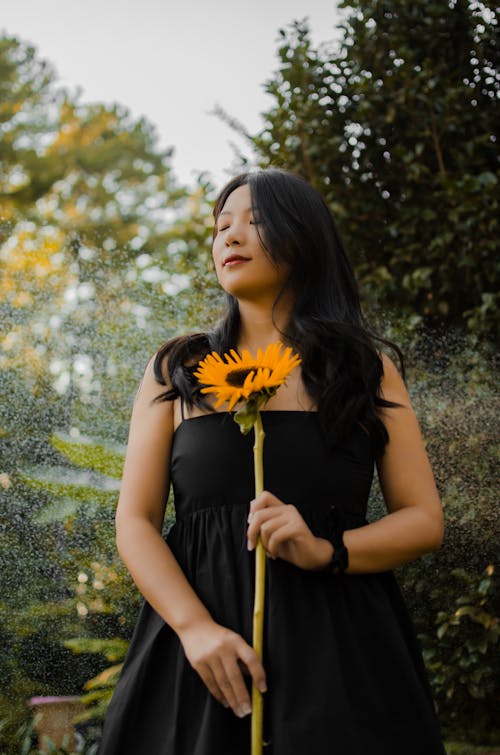 Brunette Woman in Black Strap Dress Posing in a Park with Sunflower