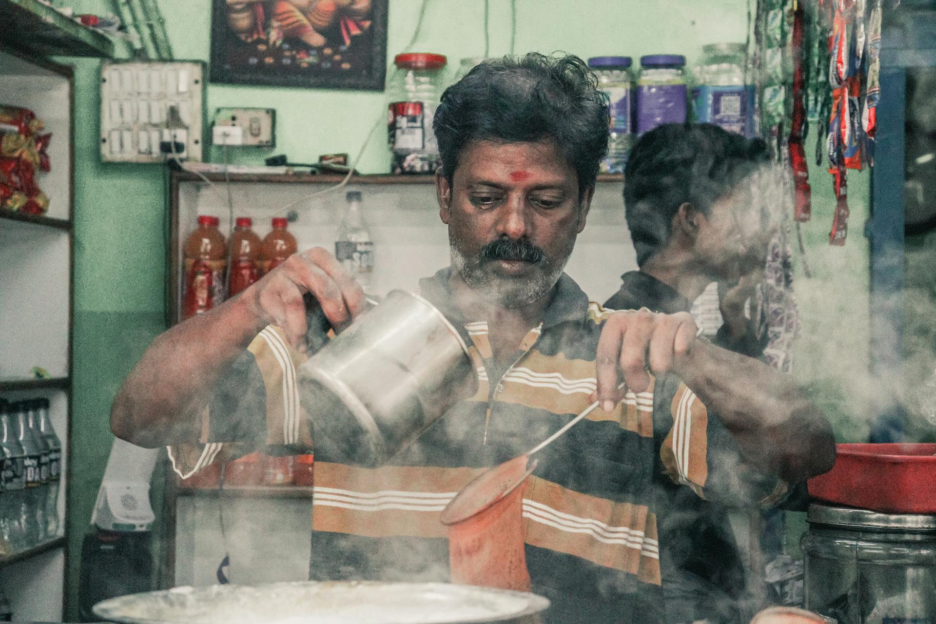 A man pouring hot masala chai with steam rising, capturing a traditional Indian market scene.