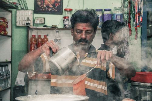 Free A man pouring hot masala chai with steam rising, capturing a traditional Indian market scene. Stock Photo