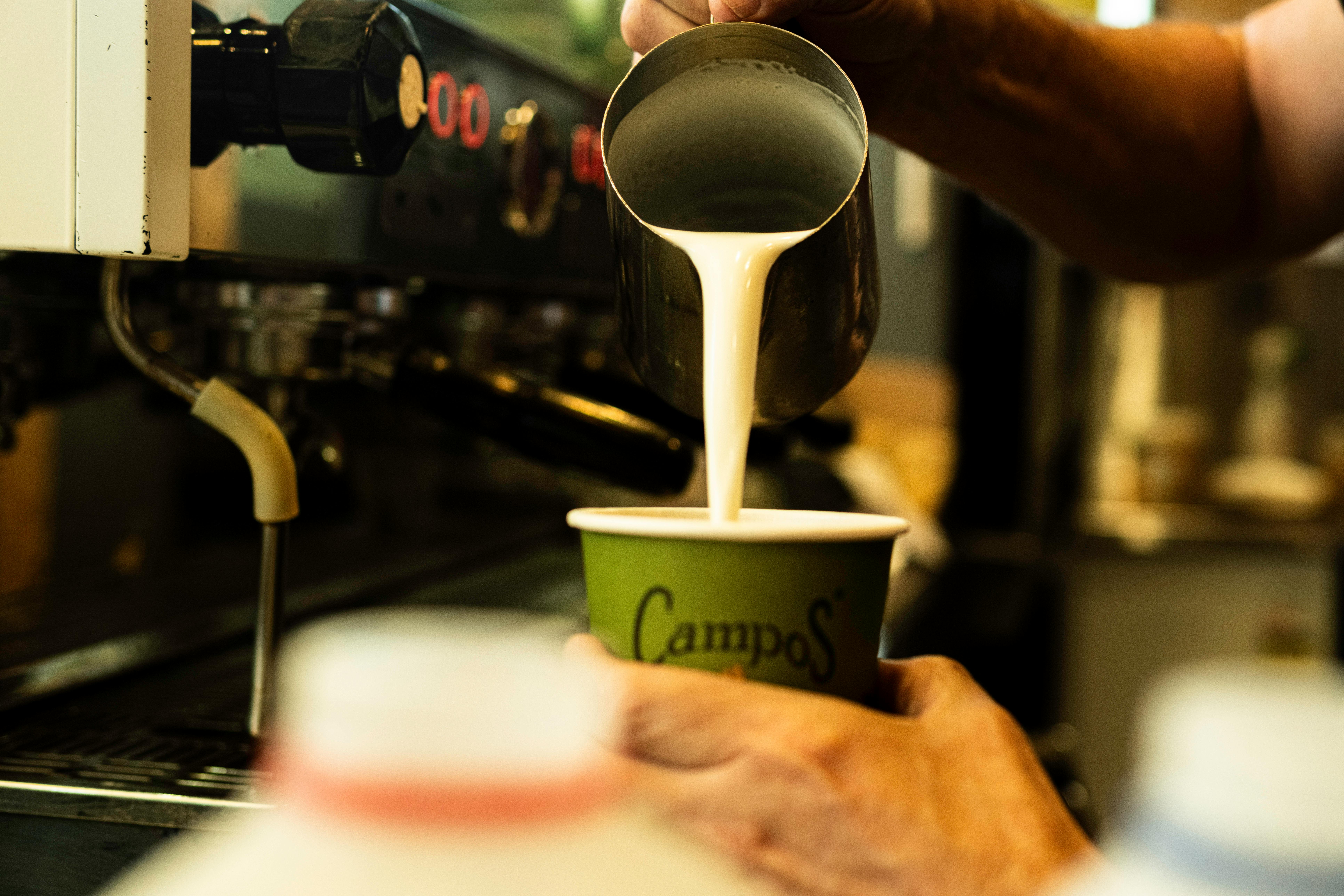 barista pouring frothed milk into a cup of coffee