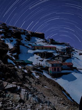Captivating snowy mountainside village with star trails illuminating the winter night sky.