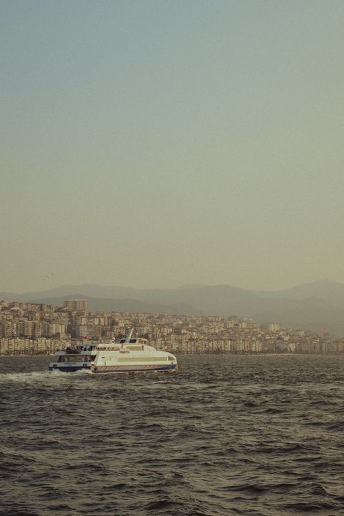 Free A ferry navigating calm waters with an urban cityscape in the background during dusk. Stock Photo