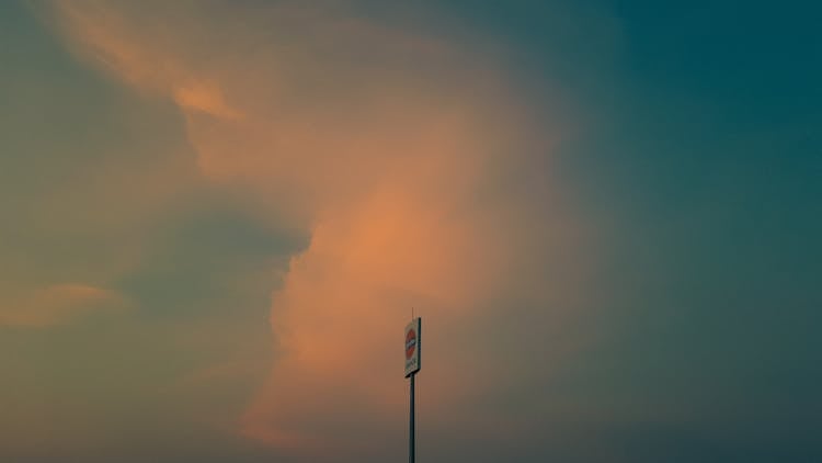 Sign With A Gas Station Logo With The Evening Sky In The Background