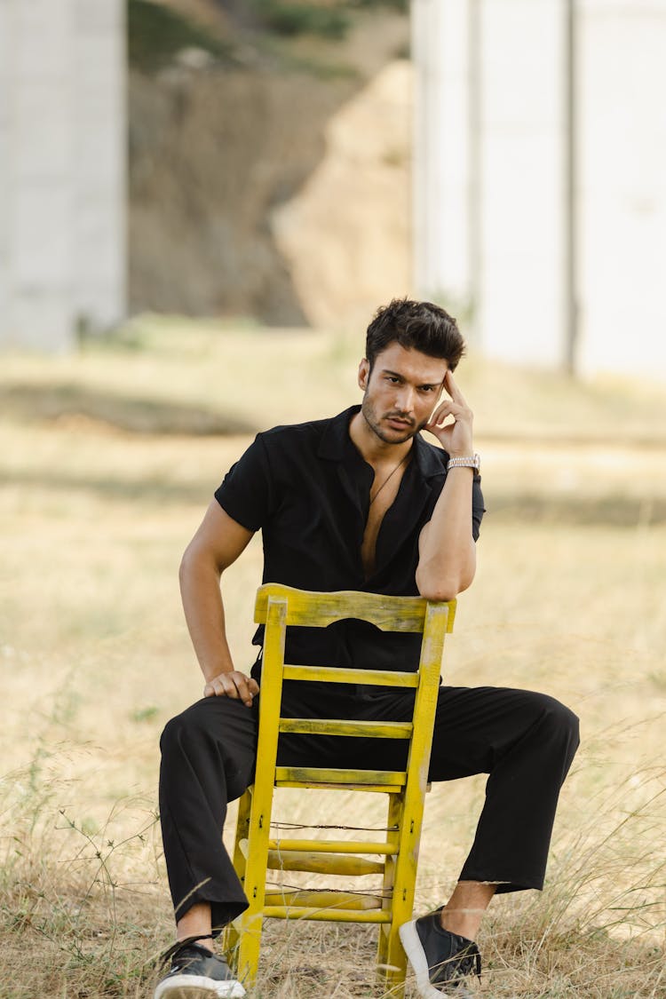 Man Sitting Backwards On A Yellow Wooden Chair Under An Overpass