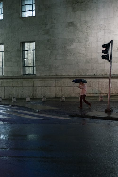 A Man Using an Umbrella Walking on the Roadside