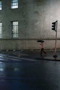 一名男子撑着伞，在雨中穿过水泥建筑旁潮湿的城市街道