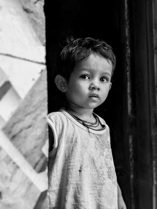 Free A thoughtful child stands in a doorway, captured in black and white, emphasizing innocence. Stock Photo