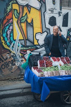 一个开朗的街头小贩在彩色壁画旁一边卖水果一边打电话