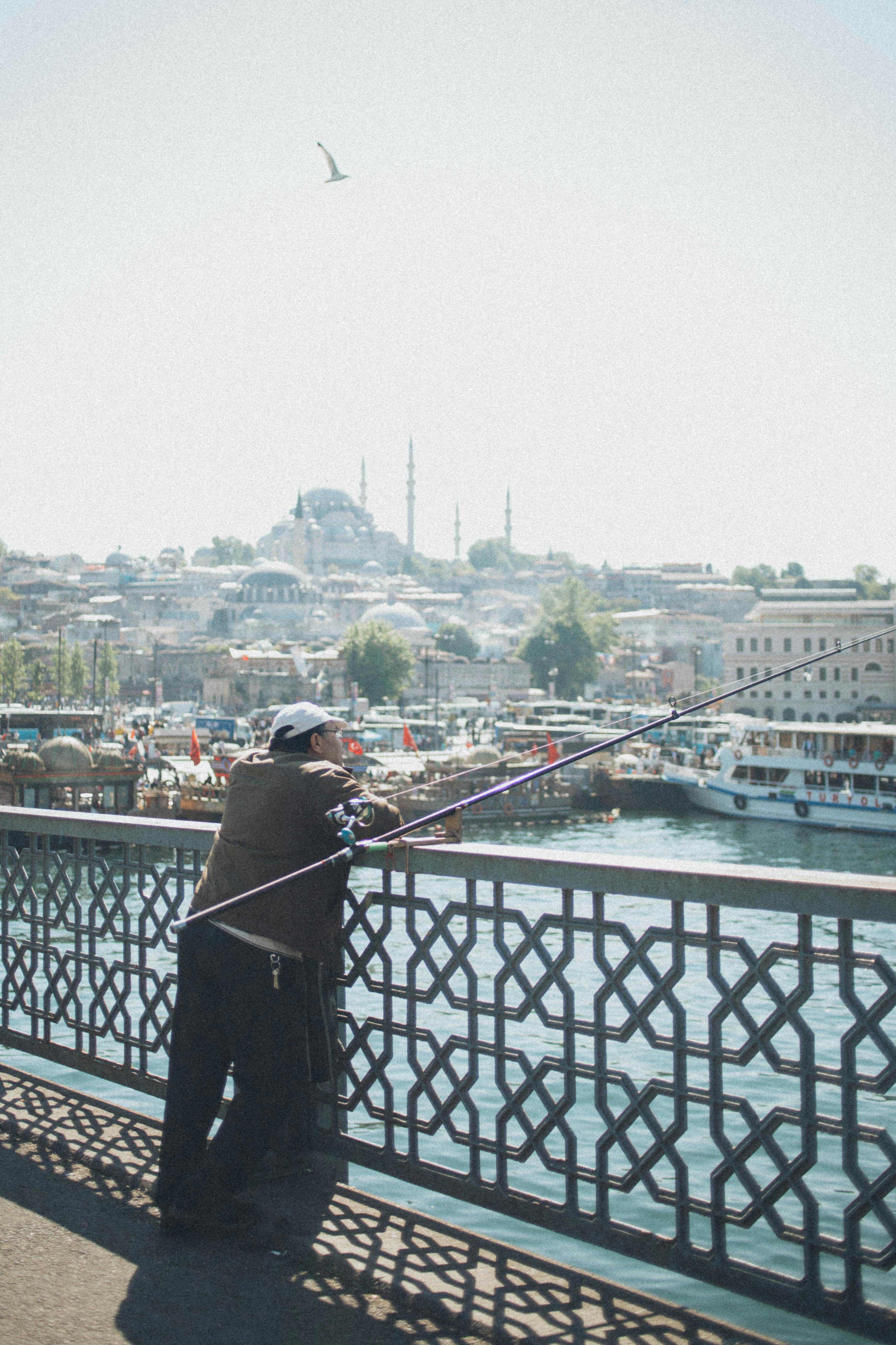 在伊斯坦布尔历史悠久的加拉塔桥上，一名男子正用钓竿钓鱼，背景是城市景观