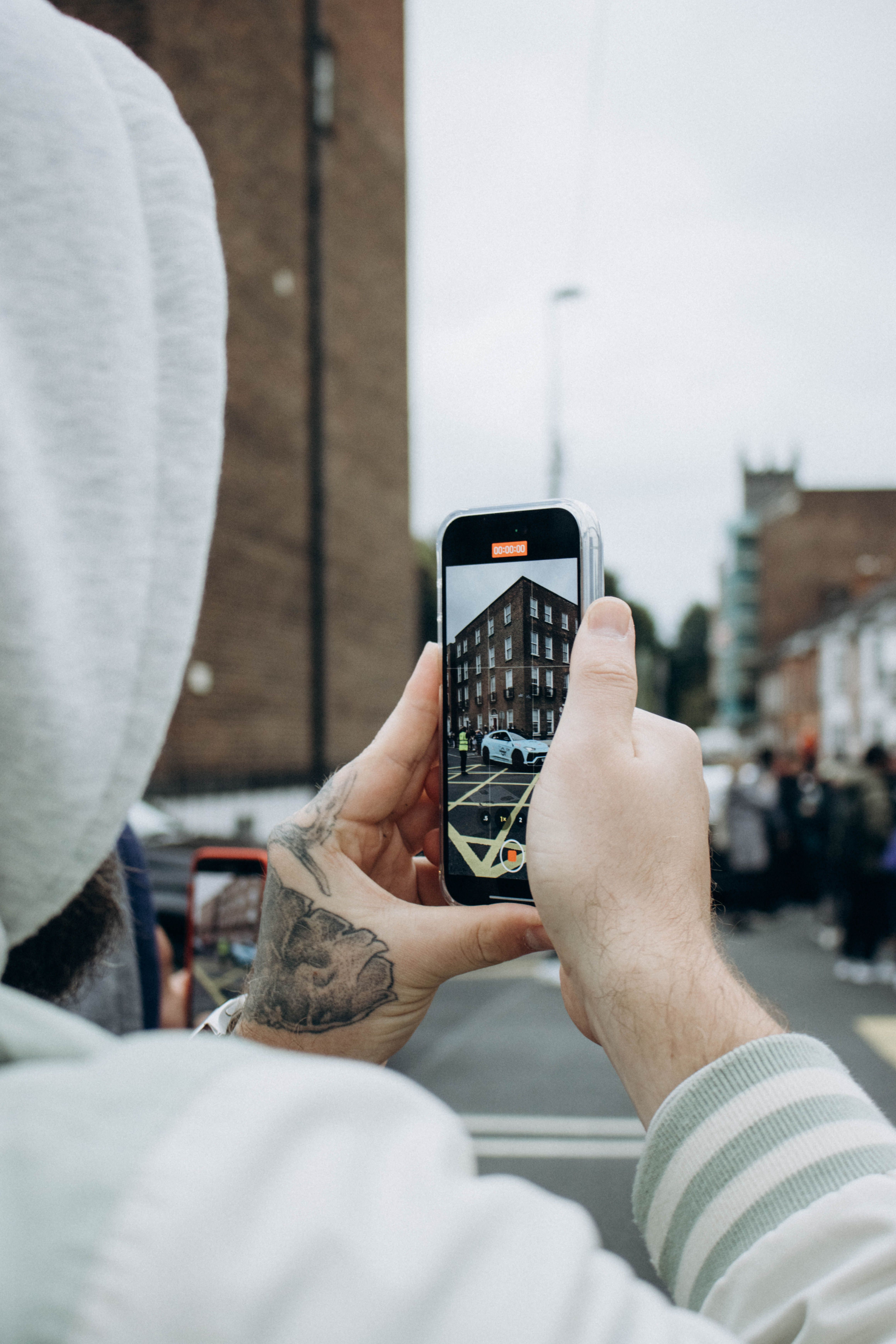 A person photographs an urban street scene with a smartphone, capturing a police car and crowd.