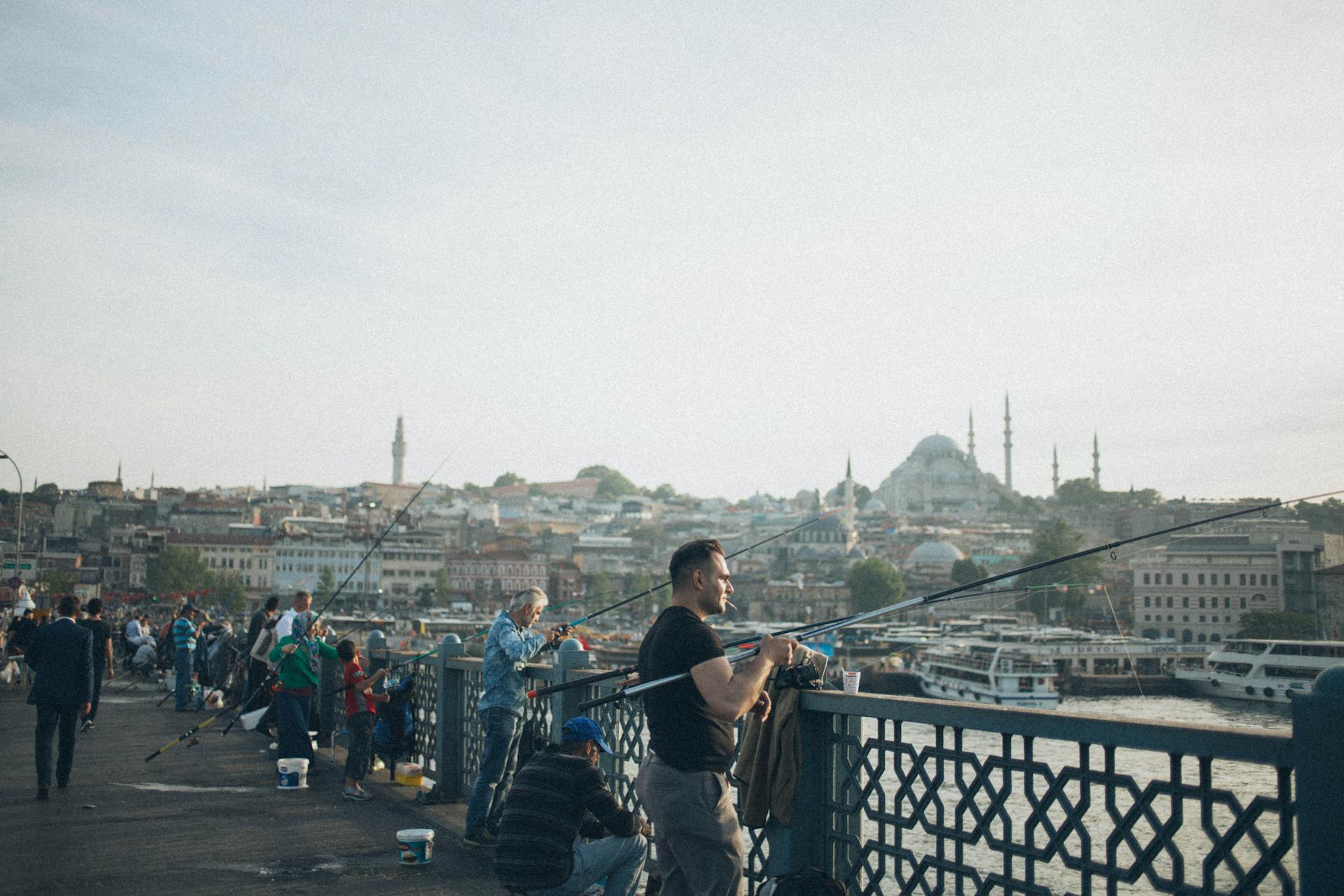 People fishing on Galata Bridge with a view of Istanbul's skyline and mosques. Perfect travel photo.