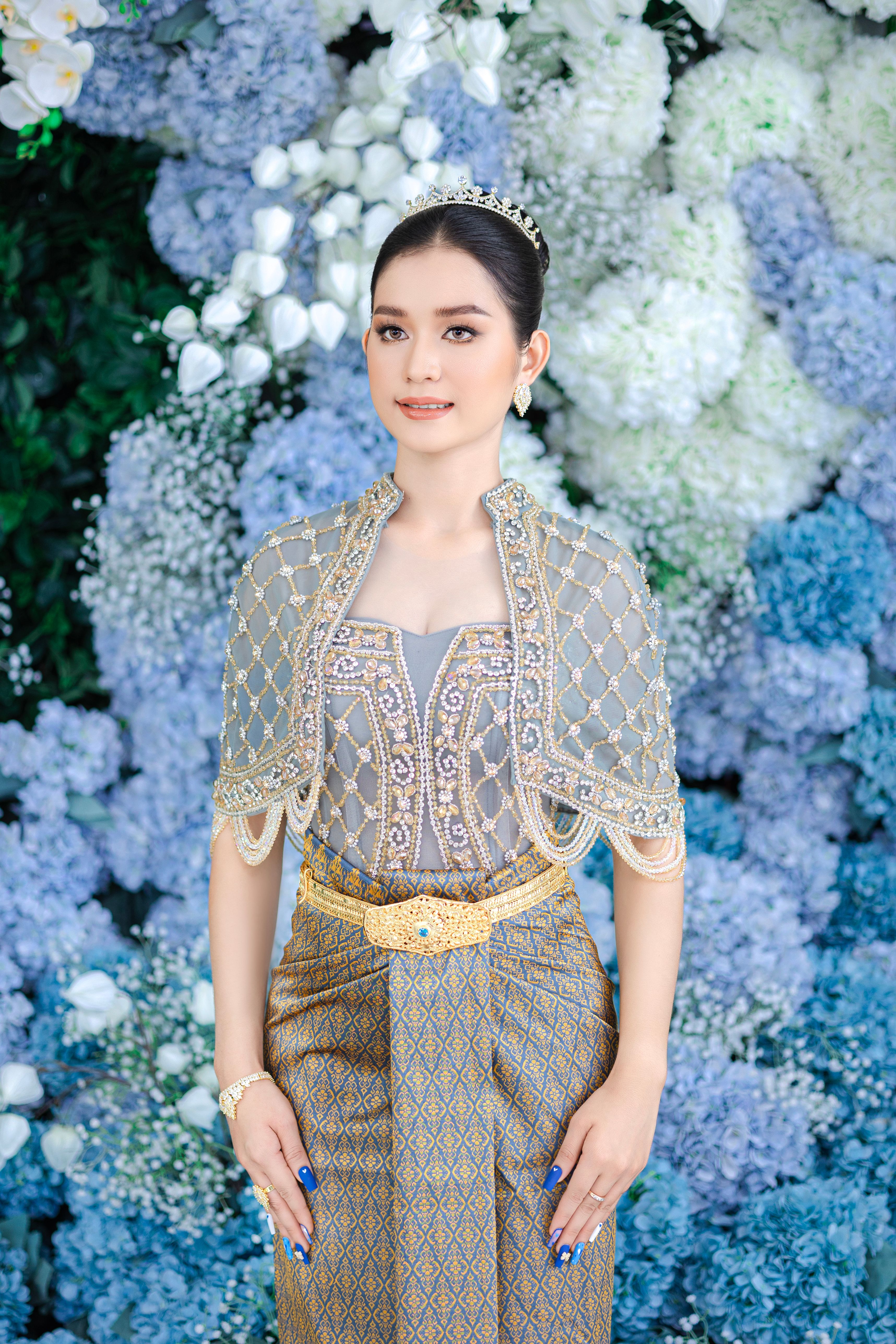 A young woman in traditional elegant attire poses with a stunning floral backdrop, exuding grace and style.