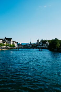 Experience Zurich's picturesque waterfront with clear skies and historical architecture reflected in the Limmat River.