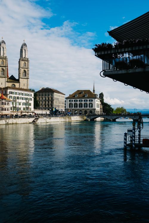 Free Beautiful view of Zurich's iconic Grossmünster church along the Limmat River on a sunny day. Stock Photo