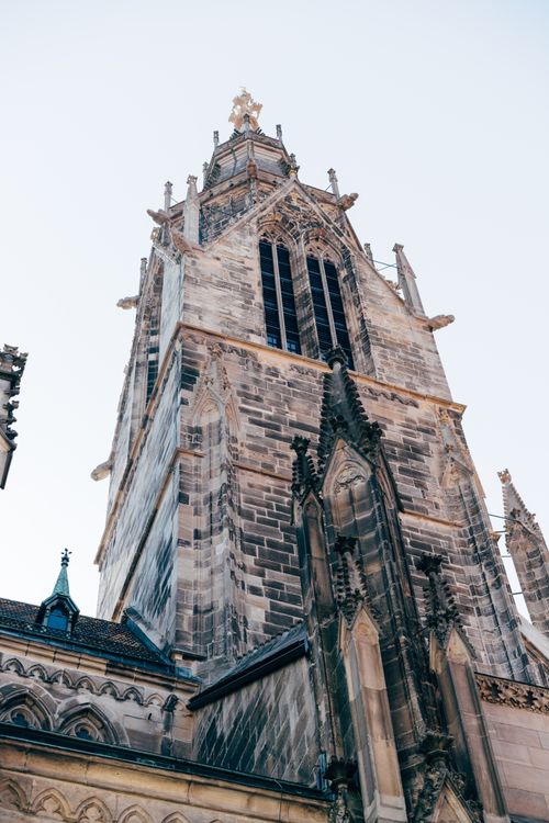 Free A stunning view of a Gothic cathedral tower with intricate architecture, under a clear sky. Stock Photo