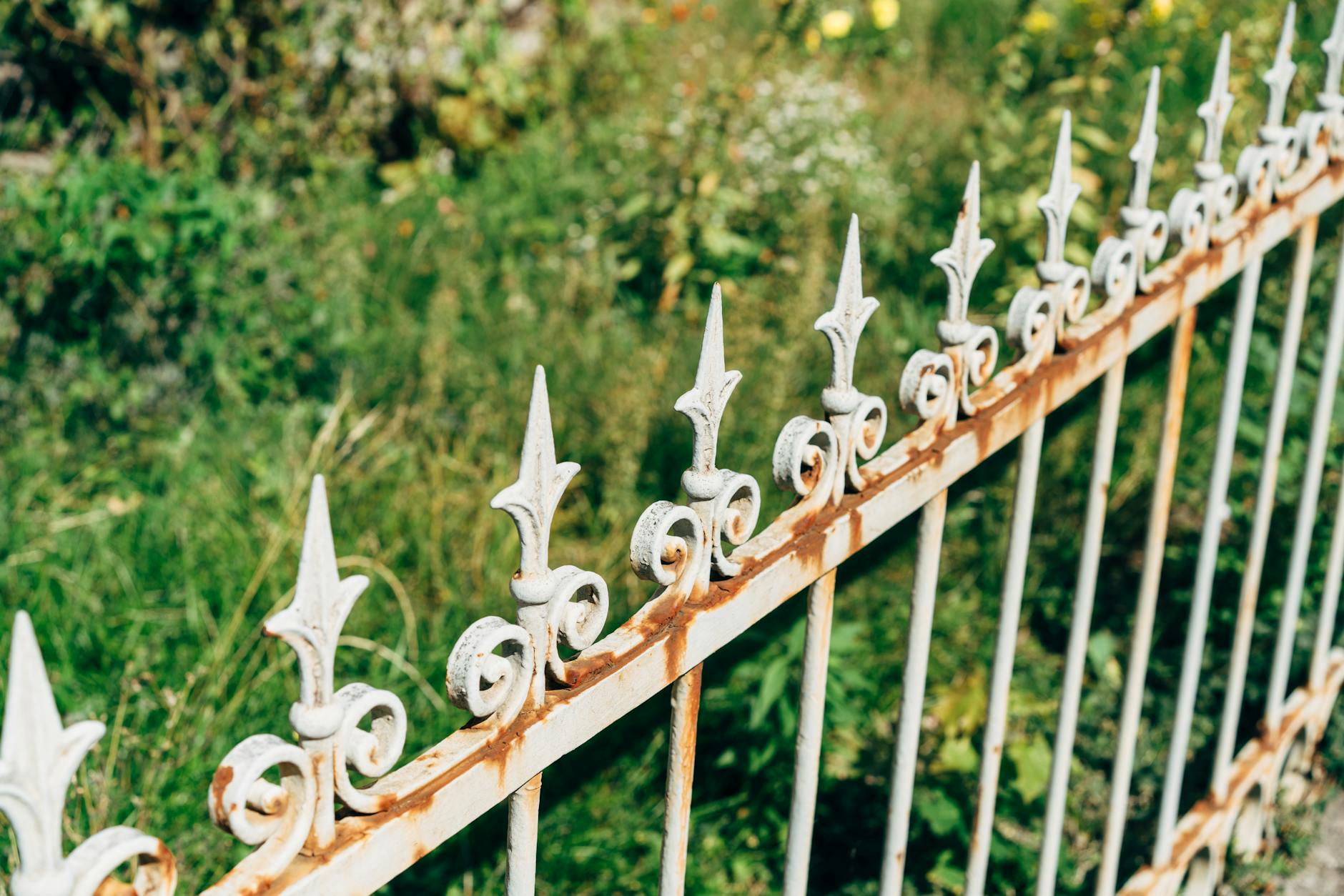 A detailed view of an ornate, rusty fence against a vibrant garden backdrop, showcasing classic design elements.