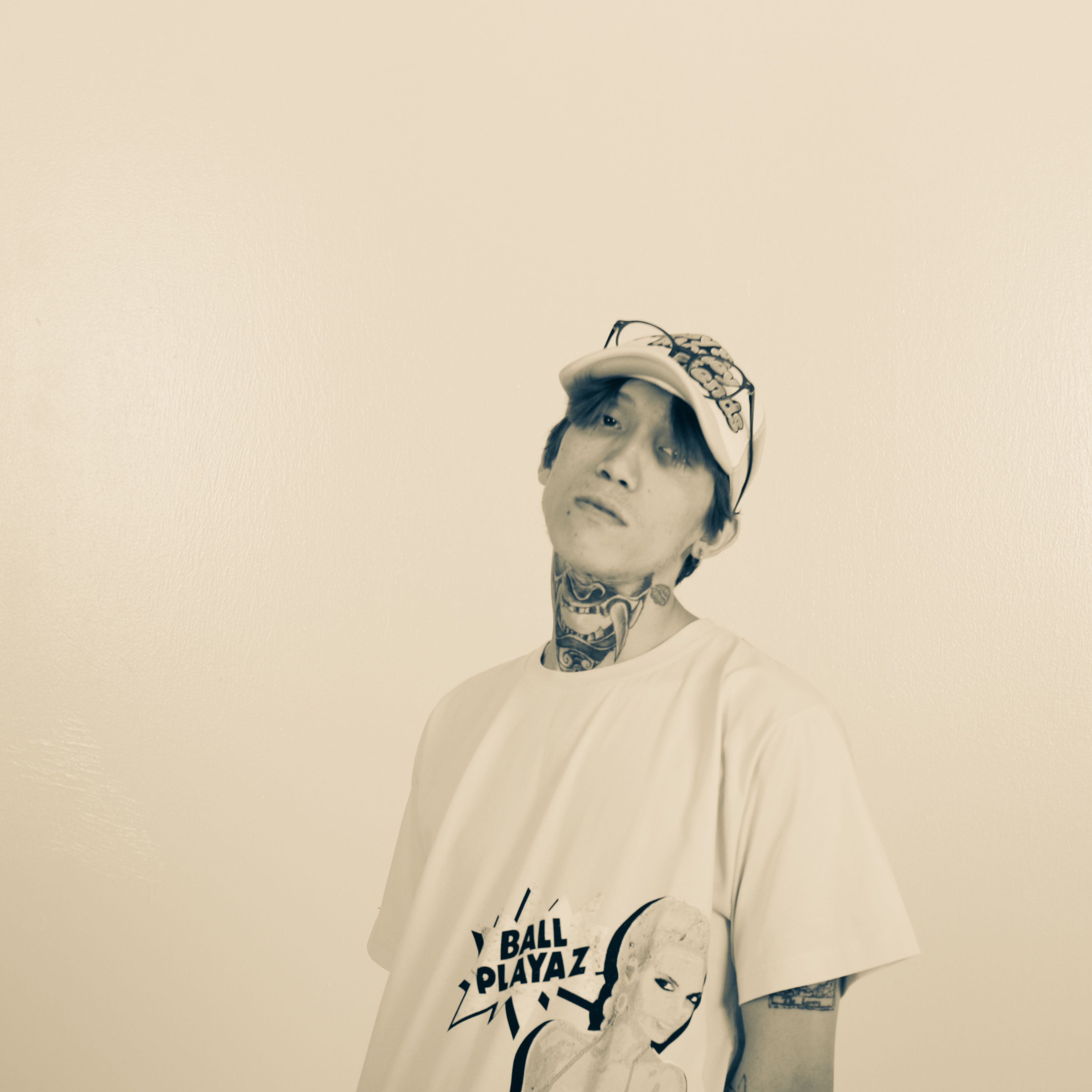 A stylish monochrome portrait of a tattooed young man wearing a baseball cap and graphic t-shirt.