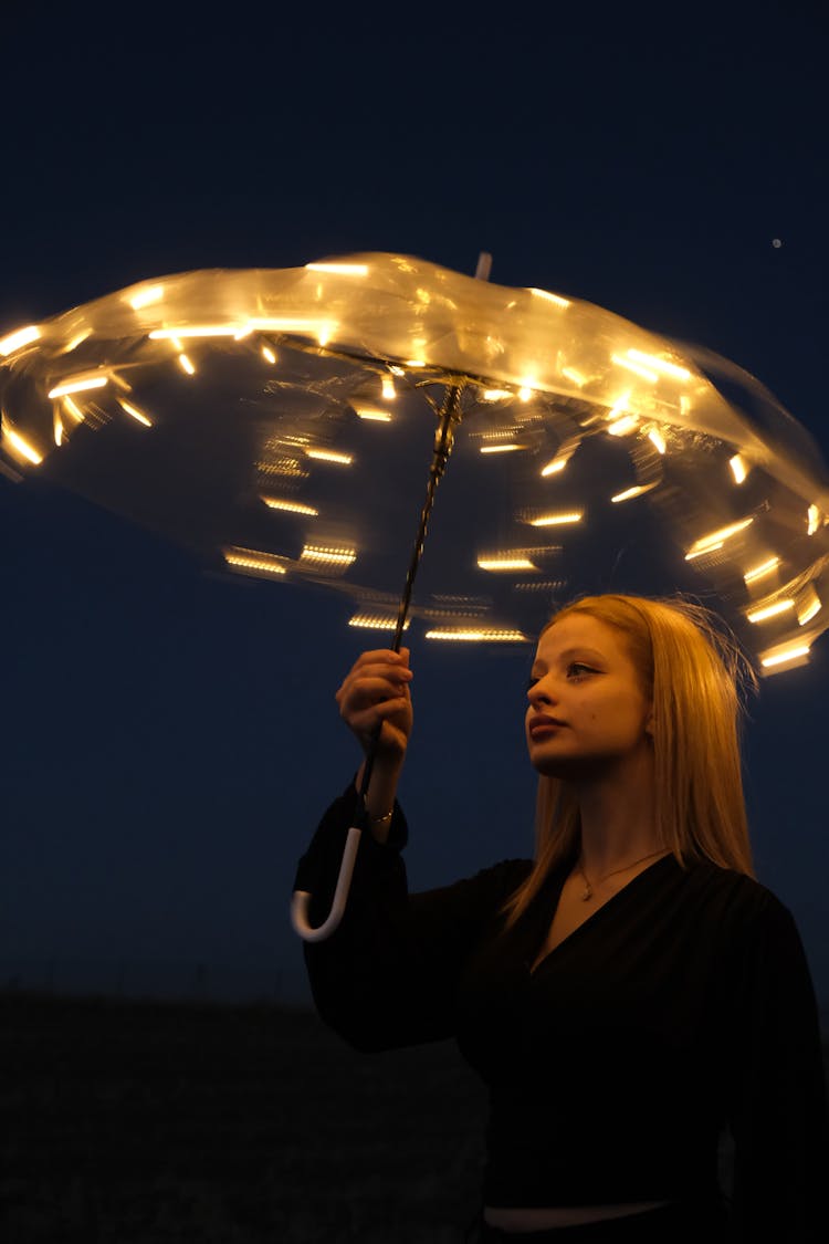 Young Blonde Woman In Black Blouse Spinning Umbrella With LED Lamps