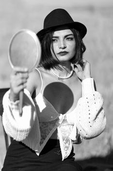 Stylish woman in hat poses with mirror, emphasizing elegance and fashion.