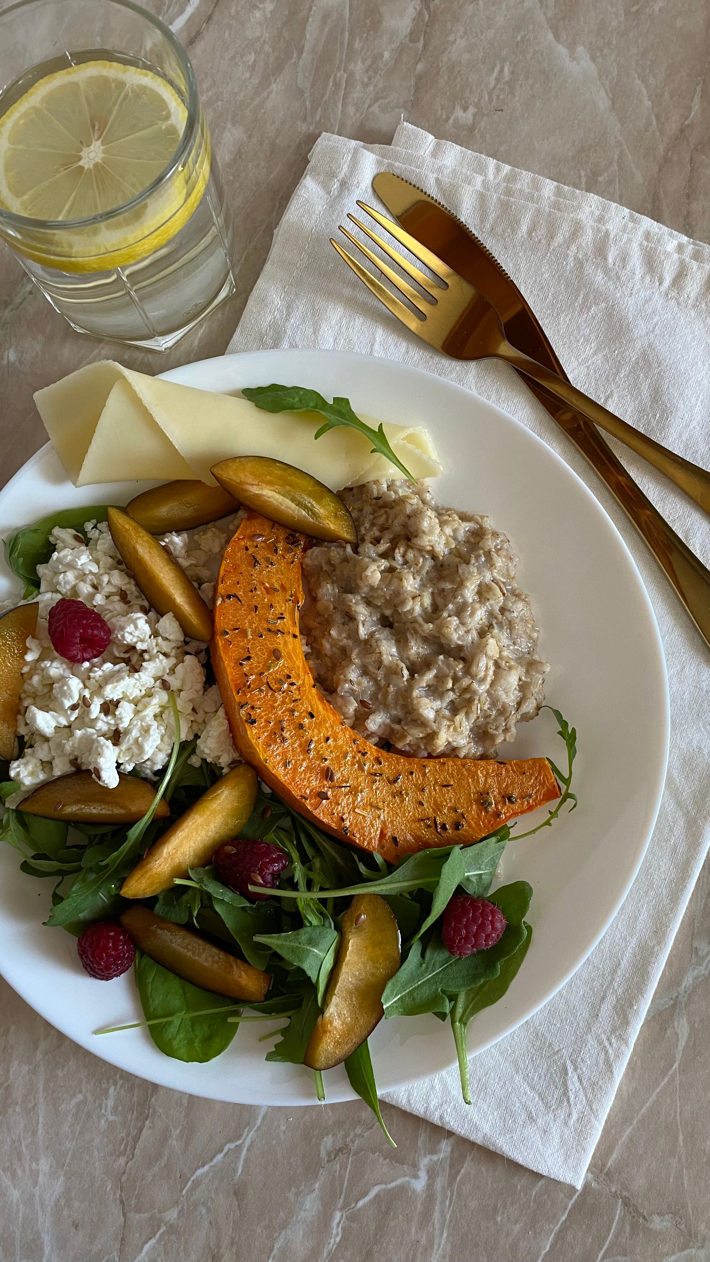 A gourmet salad featuring pumpkin, arugula, raspberries, and cottage cheese on a marble table.