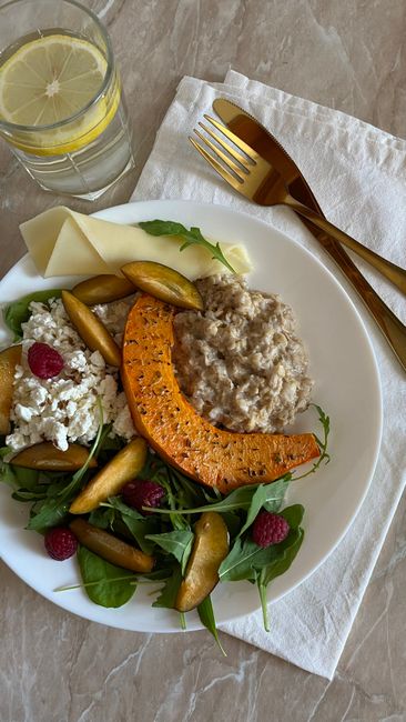 A gourmet salad featuring pumpkin, arugula, raspberries, and cottage cheese on a marble table.