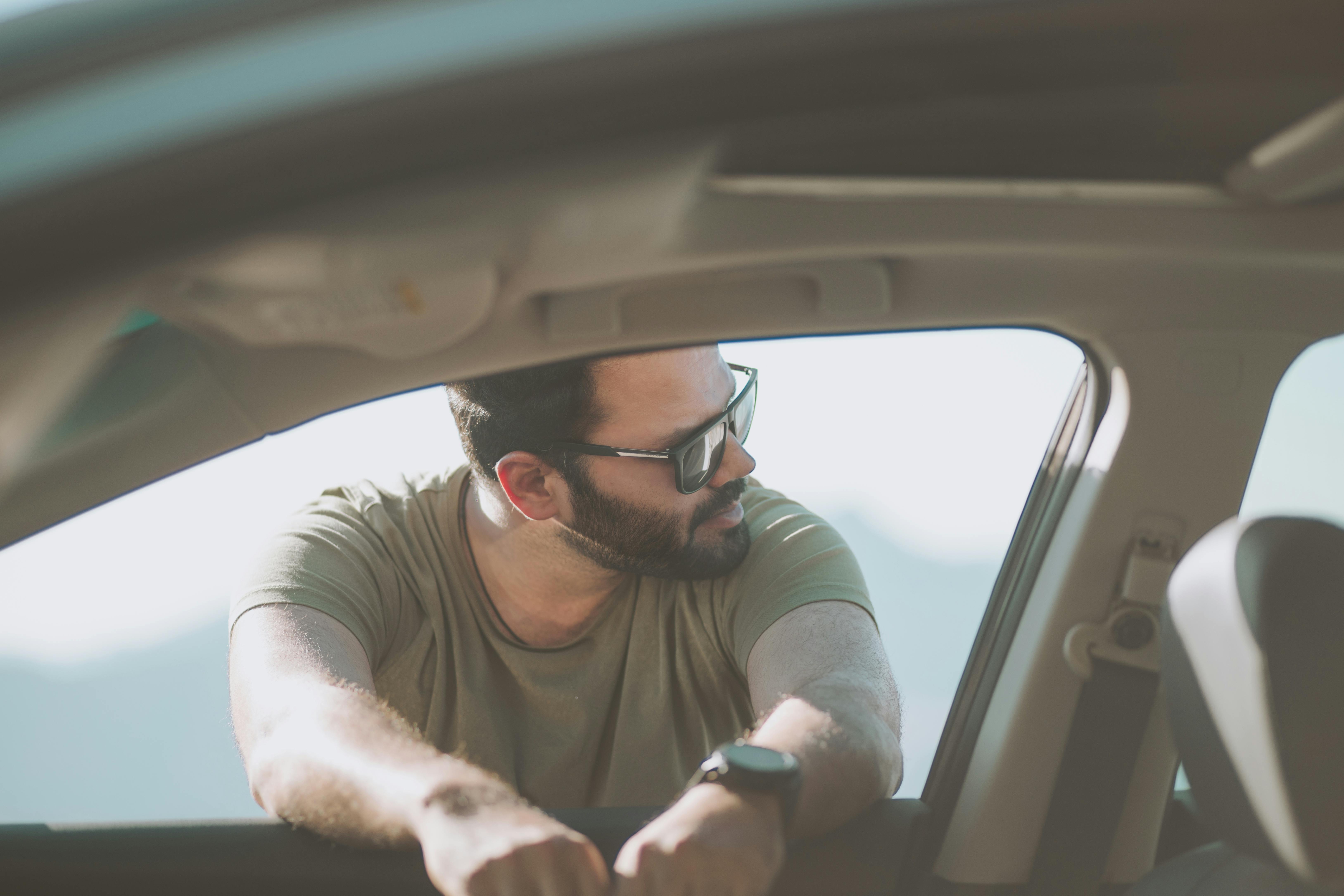 Free A man with sunglasses and a beard leans casually on a car door in Hatta, Dubai. Stock Photo