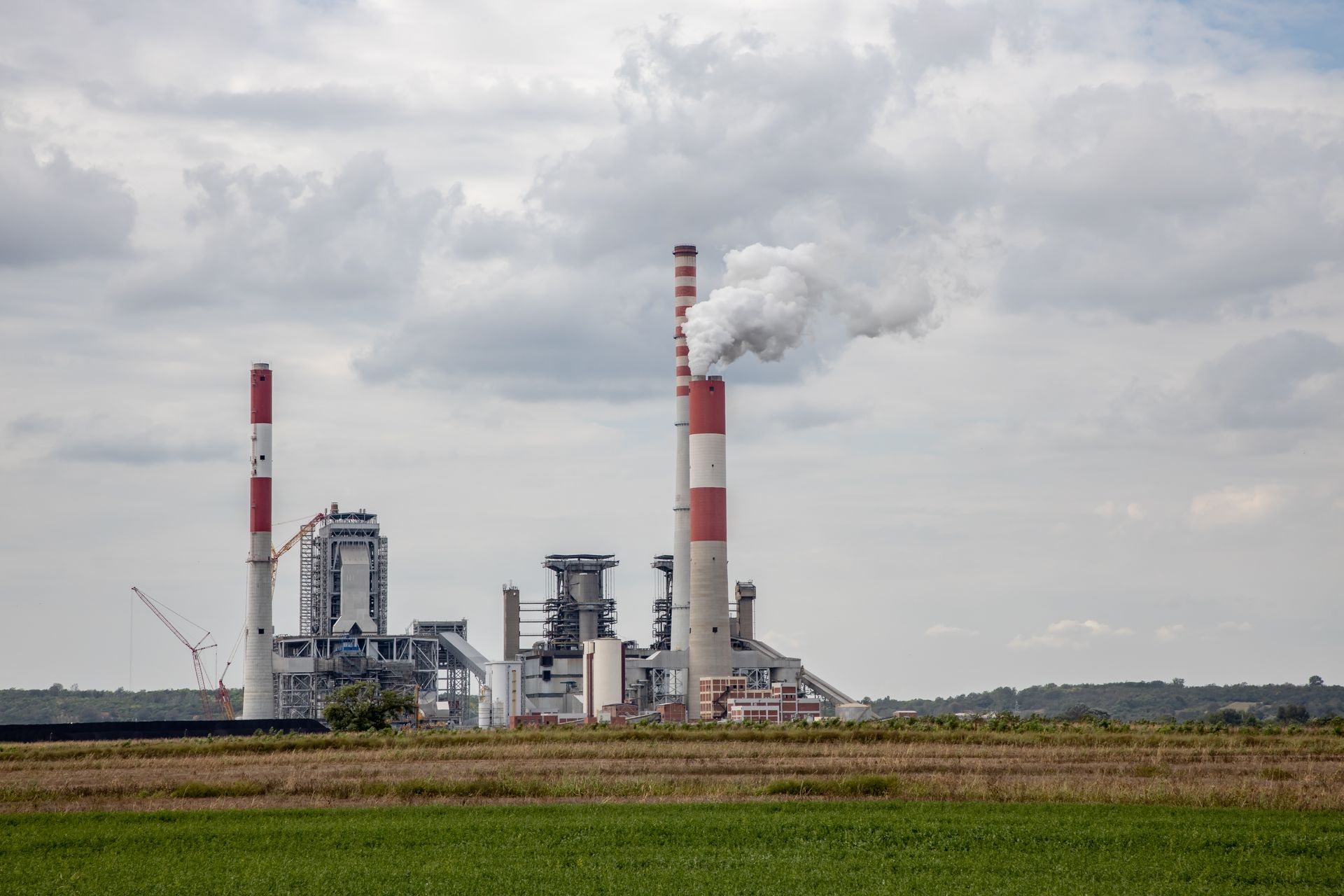 A scenic view of a power plant with smokestacks emitting smoke, set against a cloudy sky.
