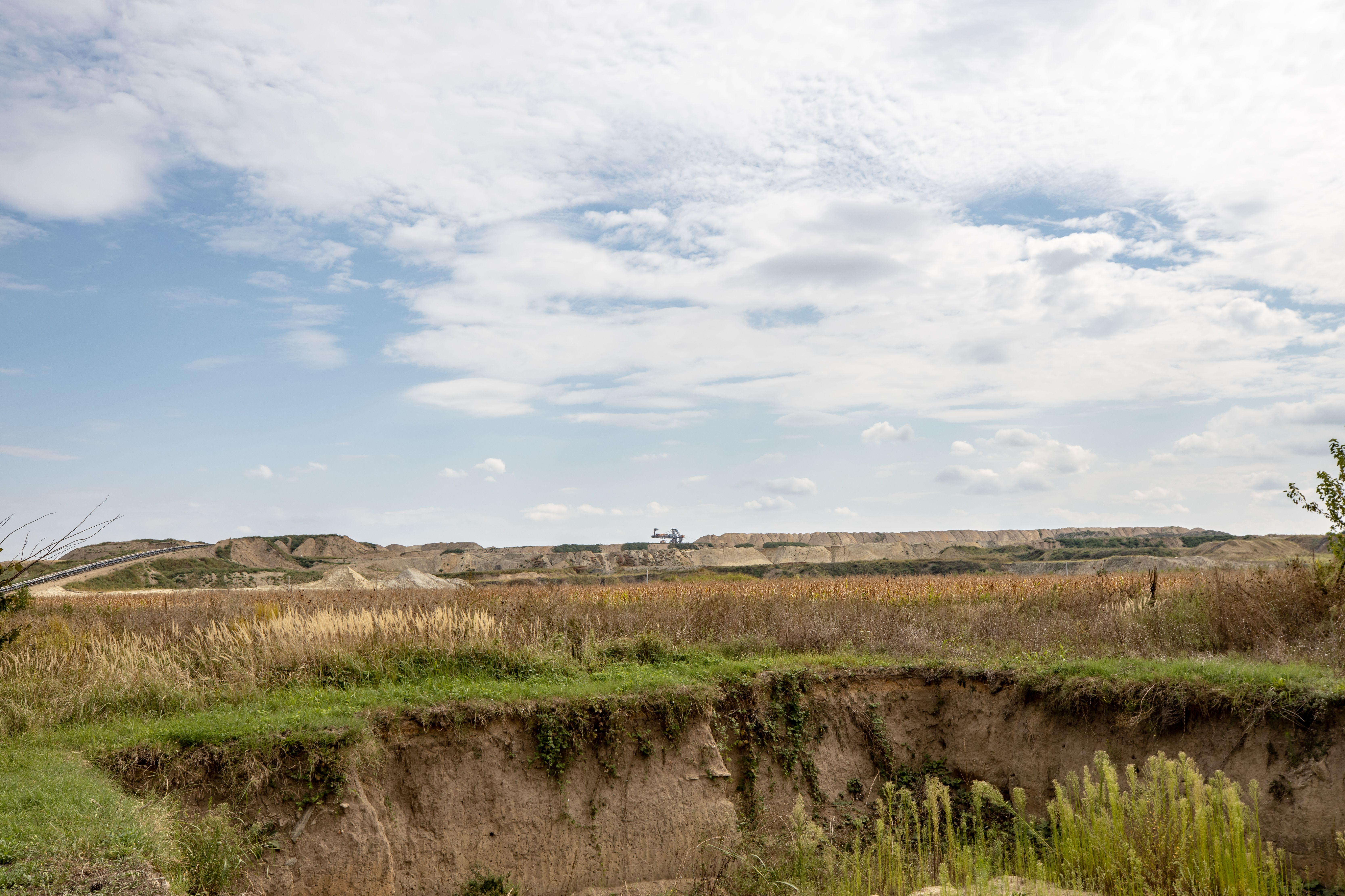Expansive rural landscape featuring excavated earth and lush pastures under a bright summer sky.