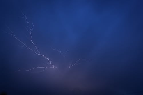 Lightning strikes over the ocean in a dark blue sky