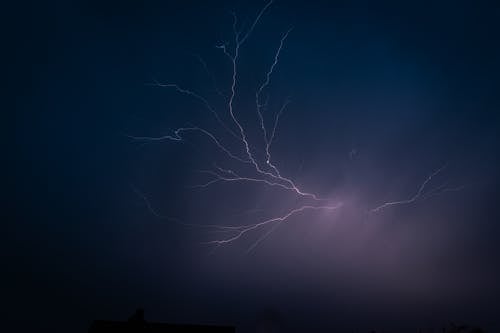 Lightning strikes over a dark sky with a house in the background
