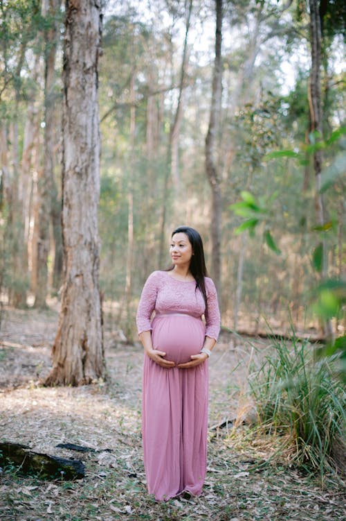 Pregnant Woman in Pink Maternity Dress Posing in the Forest