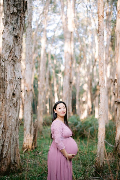 Pregnant Woman in Lilac Maternity Dress Standing in a Park