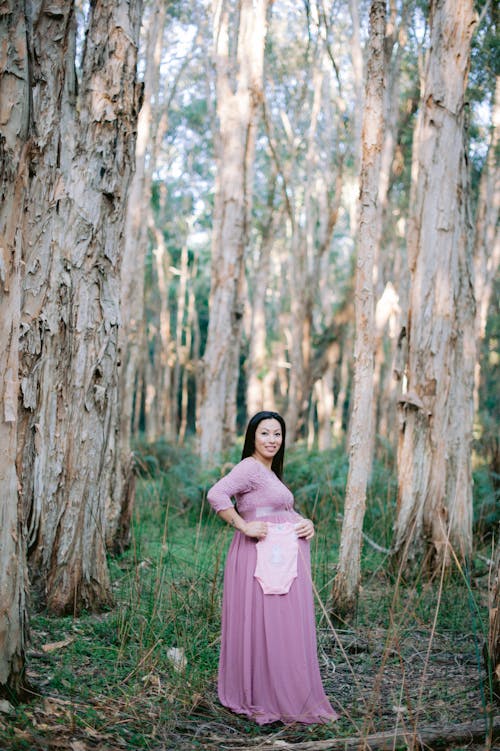 Pregnant Woman in the Forest Holding Pink Baby Rompers