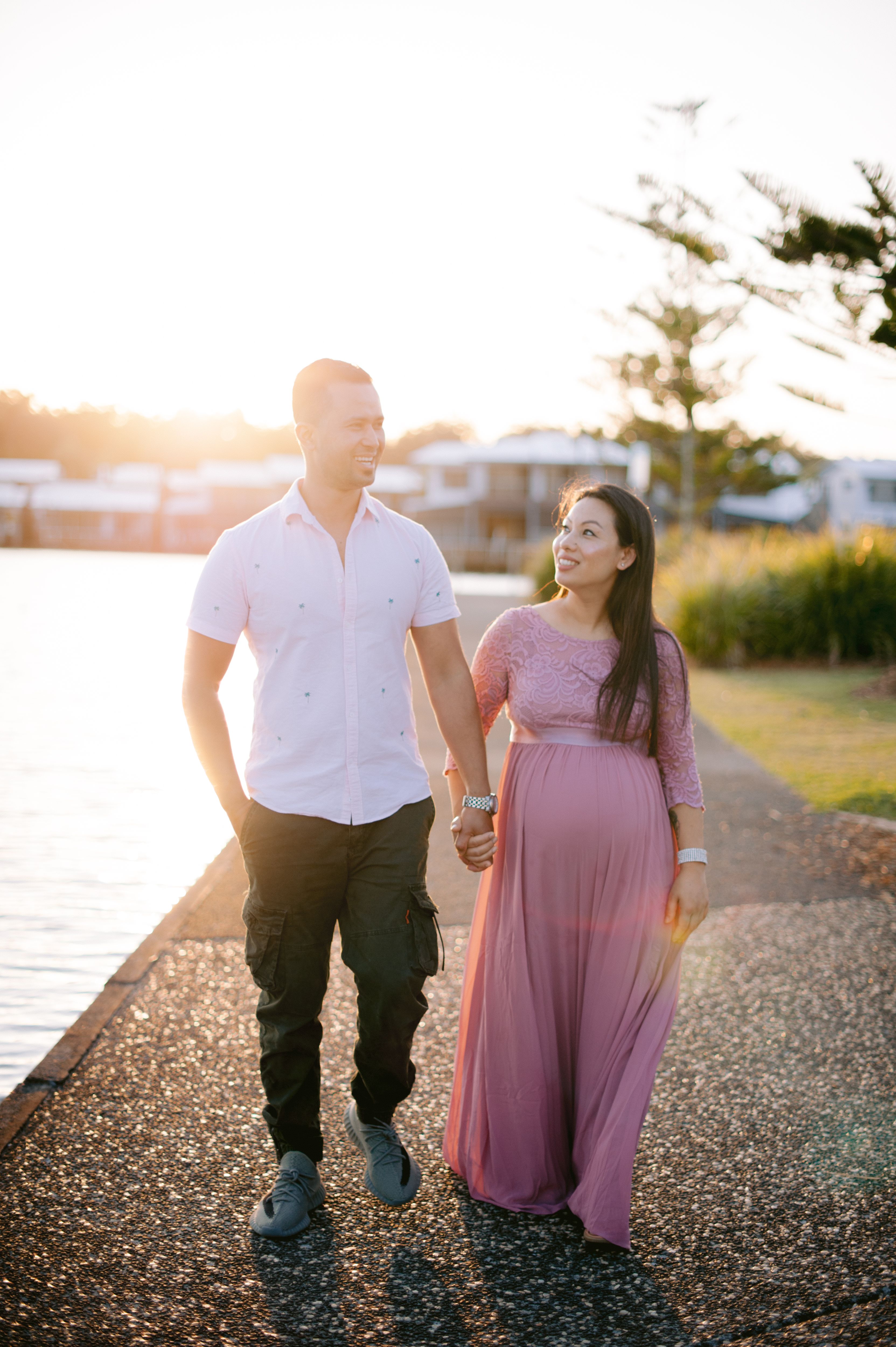 Happy pregnant couple walking by a lakeside at sunset, enjoying moments of togetherness.